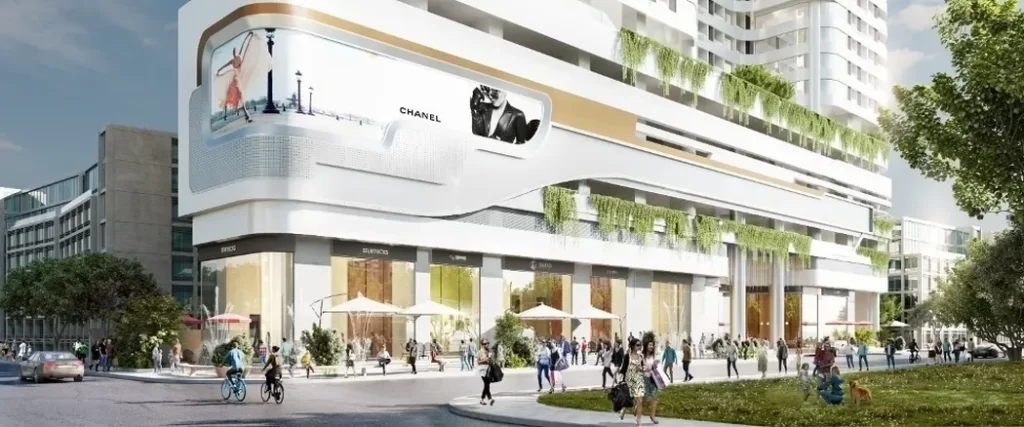 Street view of a modern multi-story building with large digital ads, greenery, outdoor seating, shops at street level, and studio apartment for rent signs—people walk by on a sunny day, creating a vibrant urban atmosphere.