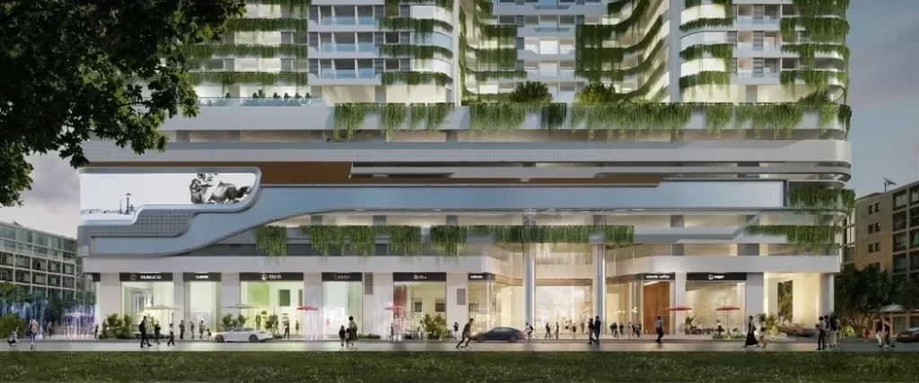 A modern multi-story building with studio apartments for rent, greenery cascading from balconies, ground-floor shops, people walking, and a car parked in front. The facade features sleek lines and an outdoor sculpture on the left side.
