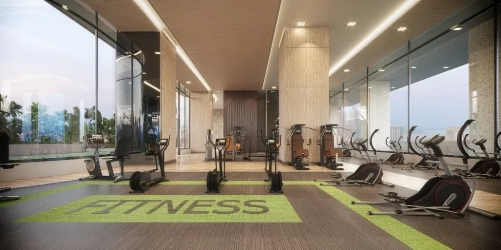 A modern gym in a studio apartment for fitness enthusiasts, featuring large windows, various cardio machines like treadmills, stationary bikes, and ellipticals, with FITNESS written on the floor in the center.
