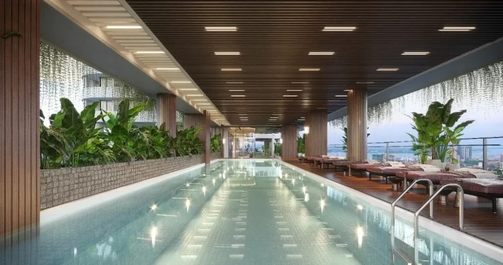 Rooftop infinity pool with modern wooden ceiling, lush green plants, and lounge chairs offers city views through glass railings—perfect for relaxing or unwinding after a day in your studio apartment for a truly luxurious lifestyle.