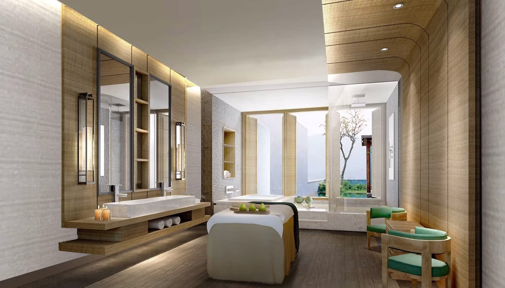 A modern spa room in a studio unit for sale, featuring a massage table, double sinks with large mirrors, shelves with towels, a seating area with green cushions, and large windows overlooking serene trees and water.
