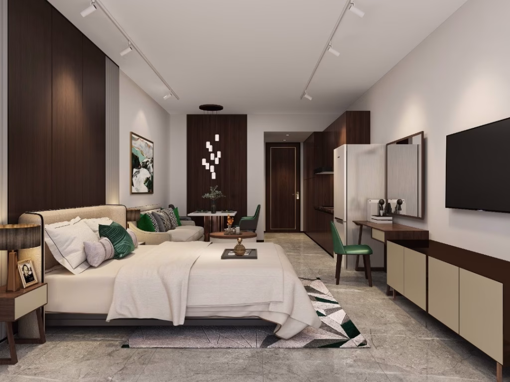 A modern Studio Unit For Sale featuring a large bed, green and beige decor, a seating area, wall art, wall-mounted TV, desk with mirror, built-in wardrobe—all set on a marble floor with soft lighting.