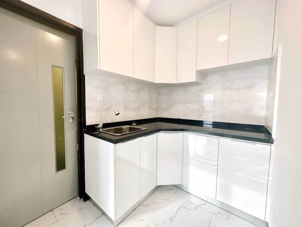 Modern 1 bed condo kitchen with white cabinets, black countertop, stainless steel sink, and silver faucet. Glossy tile floors and backsplash. Light gray door with vertical frosted glass panel is on the left.