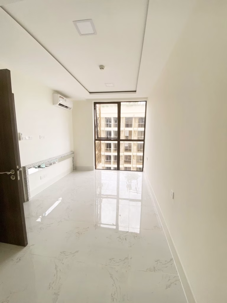 A bright, empty 1 bedroom condo featuring white marble floors, cream-colored walls, a large window with city views, an air conditioner, and a partially open wooden door.
