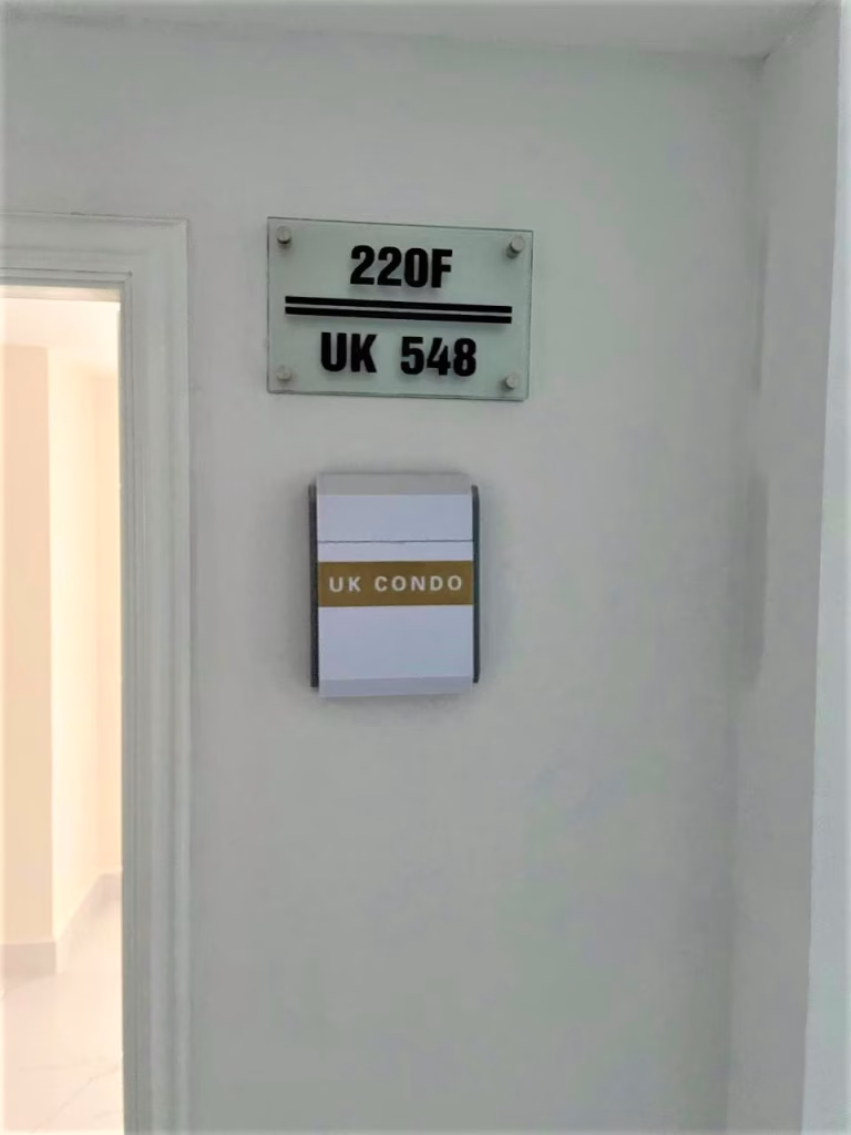 A white wall with two signs: one reads 220F UK 548 in black letters, the other, attached below, reads UK CONDO on a white and gold plaque beside an open doorway, near the unit marked UK 458.