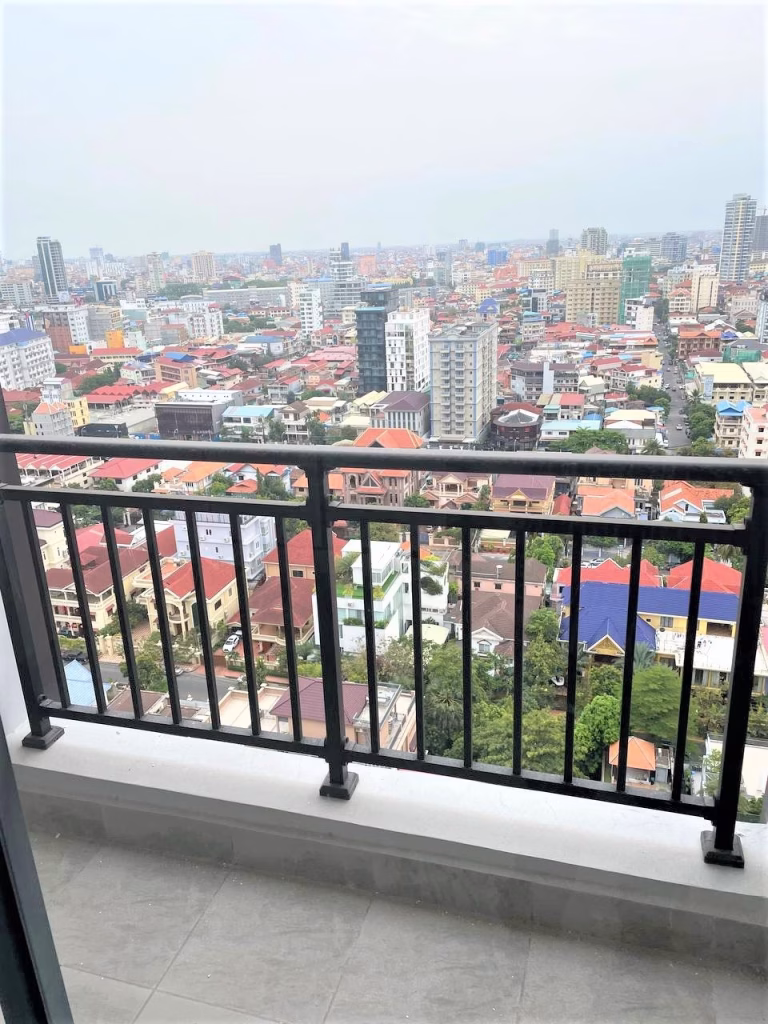 High-rise balcony view in UK 458, overlooking a cityscape of buildings, houses, and greenery under a cloudy sky. Black railing and tiled balcony floor add to the charm of this urban scene.