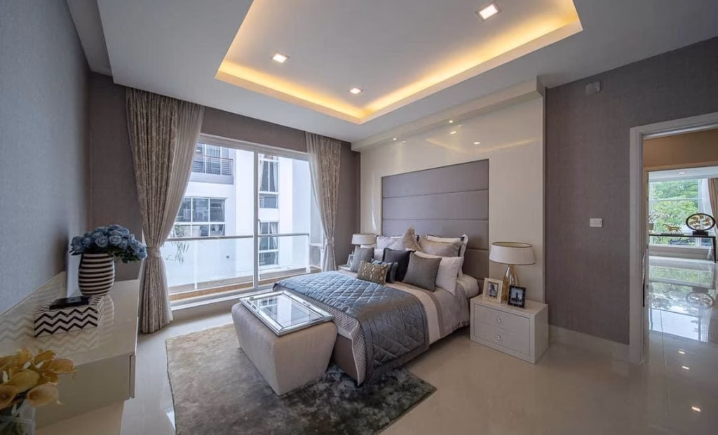 Modern, elegant bedroom in a house for sale, featuring large windows, neutral tones, gray and white bedding, bedside tables with lamps, decorative pillows, a cushioned bench at the foot of the bed, and soft ceiling lighting.