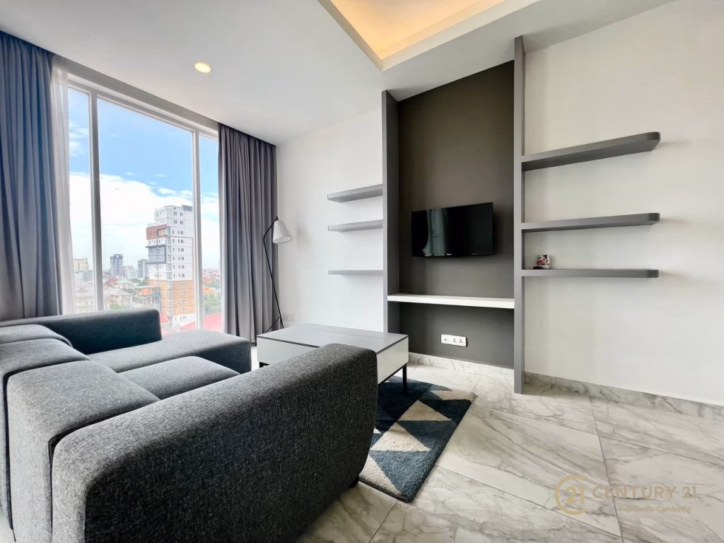 Modern living room in a studio apartment for rent, featuring a large window, gray sofa, coffee table, wall-mounted TV, floating shelves, marble floor, and cityscape view. The space is bright with natural light and minimalist decor.
