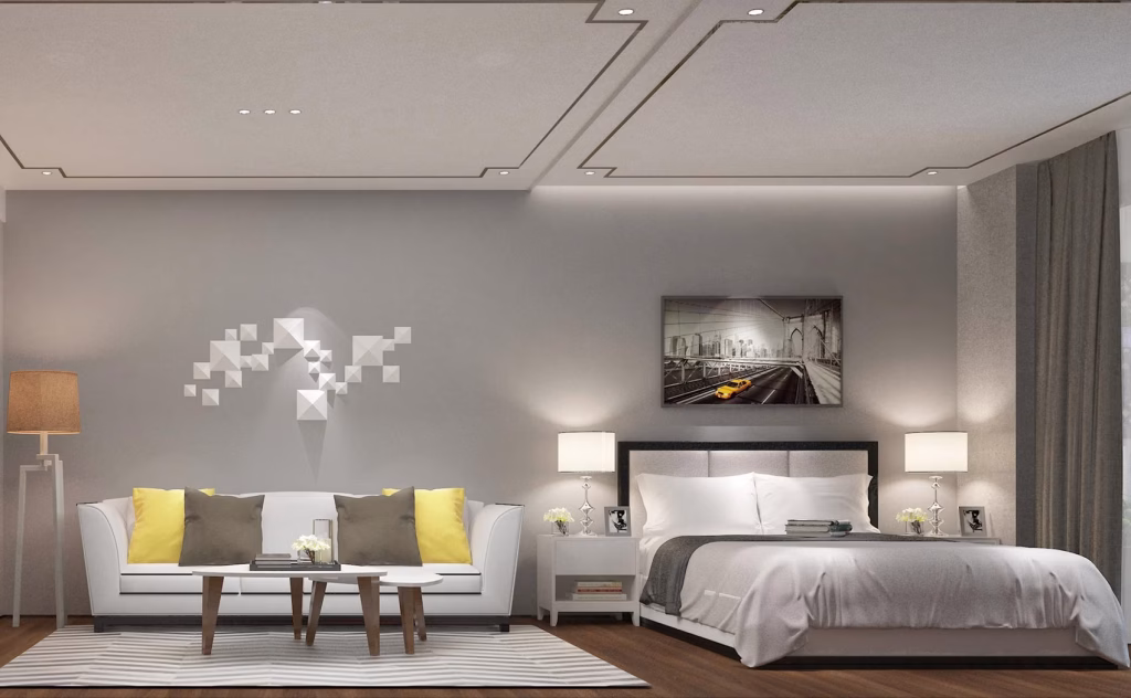 Modern bedroom at The Seagate Apartment with a white bed, grey and yellow pillows, white sofa, striped rug, bedside lamps, geometric wall decor, wall art above the bed, floor-length curtains, soft neutral tones, and wooden flooring.