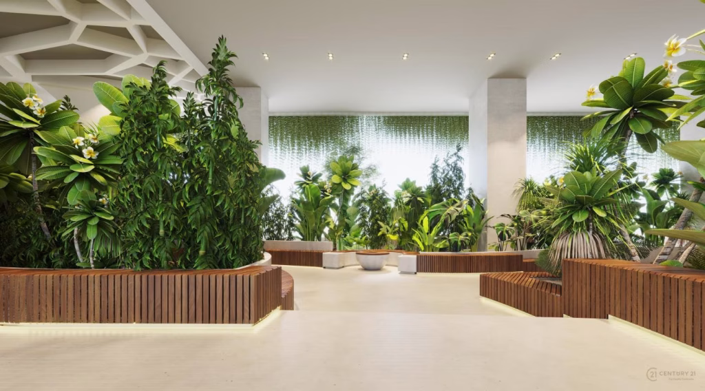 A modern indoor space at Le Condé Phnom Penh features large planters filled with lush green plants and wooden accents, complemented by a light floor and abundant natural light streaming in from tall windows in the background.