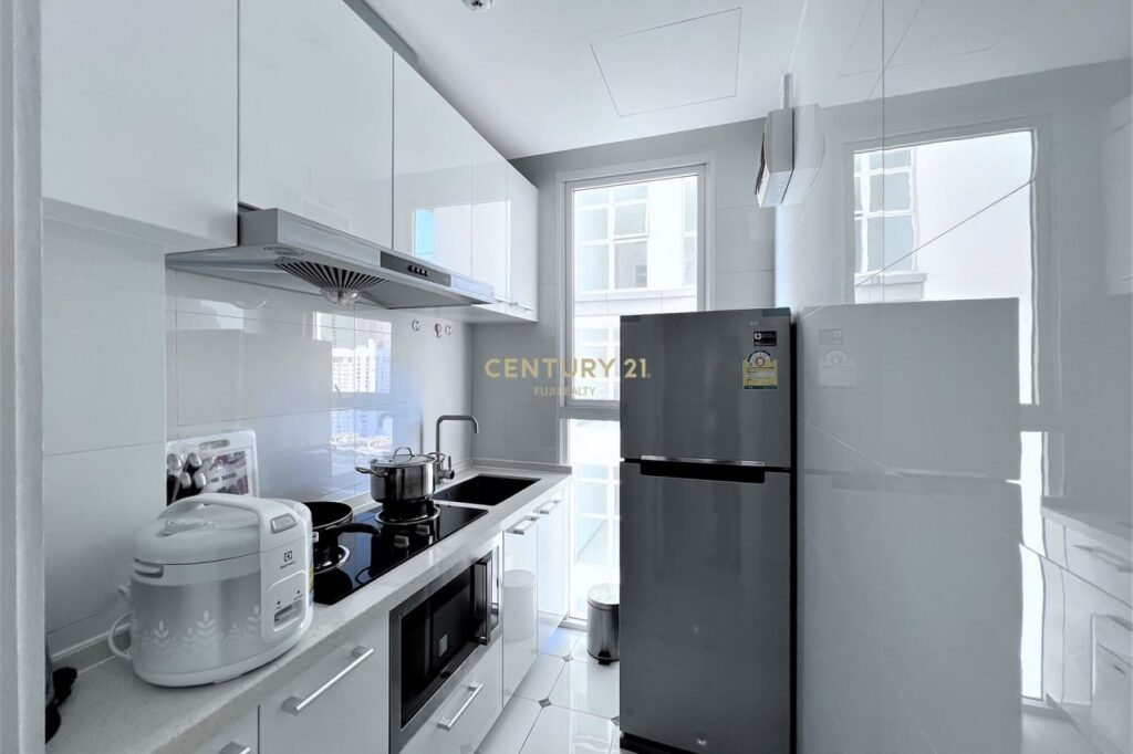 A modern, compact white kitchen in an Apartment 1 Bedroom features glossy cabinets, stainless steel appliances, a refrigerator, rice cooker, stove with pots, microwave, and a large window letting in natural light.