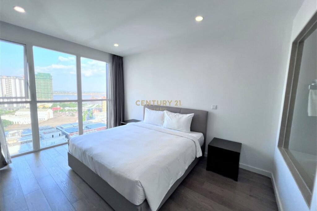Modern Apartment 1 Bedroom featuring a large bed with white bedding, dark nightstands, and floor-to-ceiling windows offering a city view. Wood flooring and white walls create a bright, clean atmosphere.