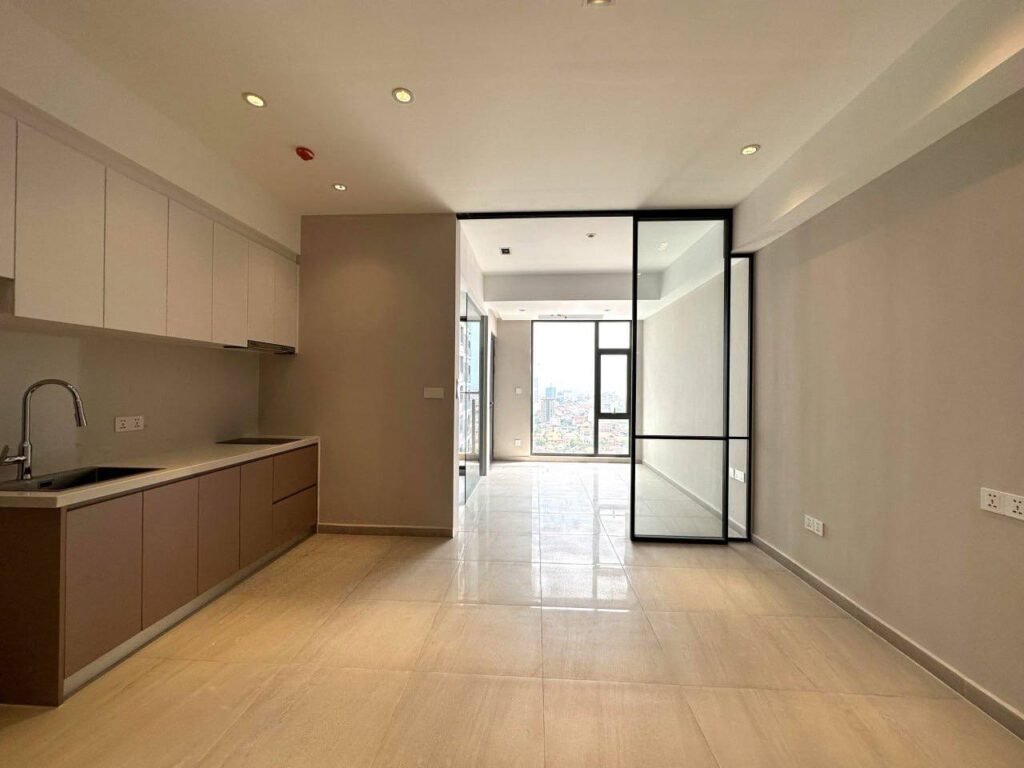 A modern, unfurnished Time Square 3 apartment kitchen and living area with beige tile floors, built-in cabinets, a sink, and large windows letting in natural light. Glass doors separate the kitchen from the living space.