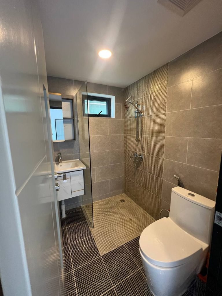 Modern bathroom with gray tiled walls and floor, featuring a glass-enclosed shower area, a white toilet, a floating sink with drawers, and a mirror cabinet above the sink. A small window is above the sink area.