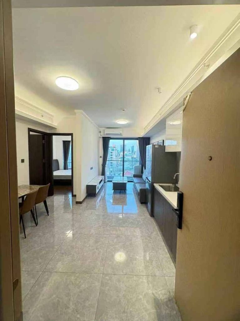 A modern apartment interior with tiled floors, a dining area on the left, a kitchenette on the right, and a living area with large windows overlooking a city skyline.